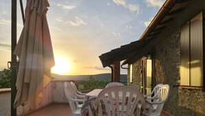 Una terraza con mesa y sillas, vista al atardecer y un edificio de piedra.