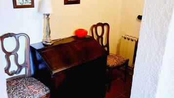 A dining area with a wooden table, two chairs, a red bowl, and framed botanical prints on the wall.