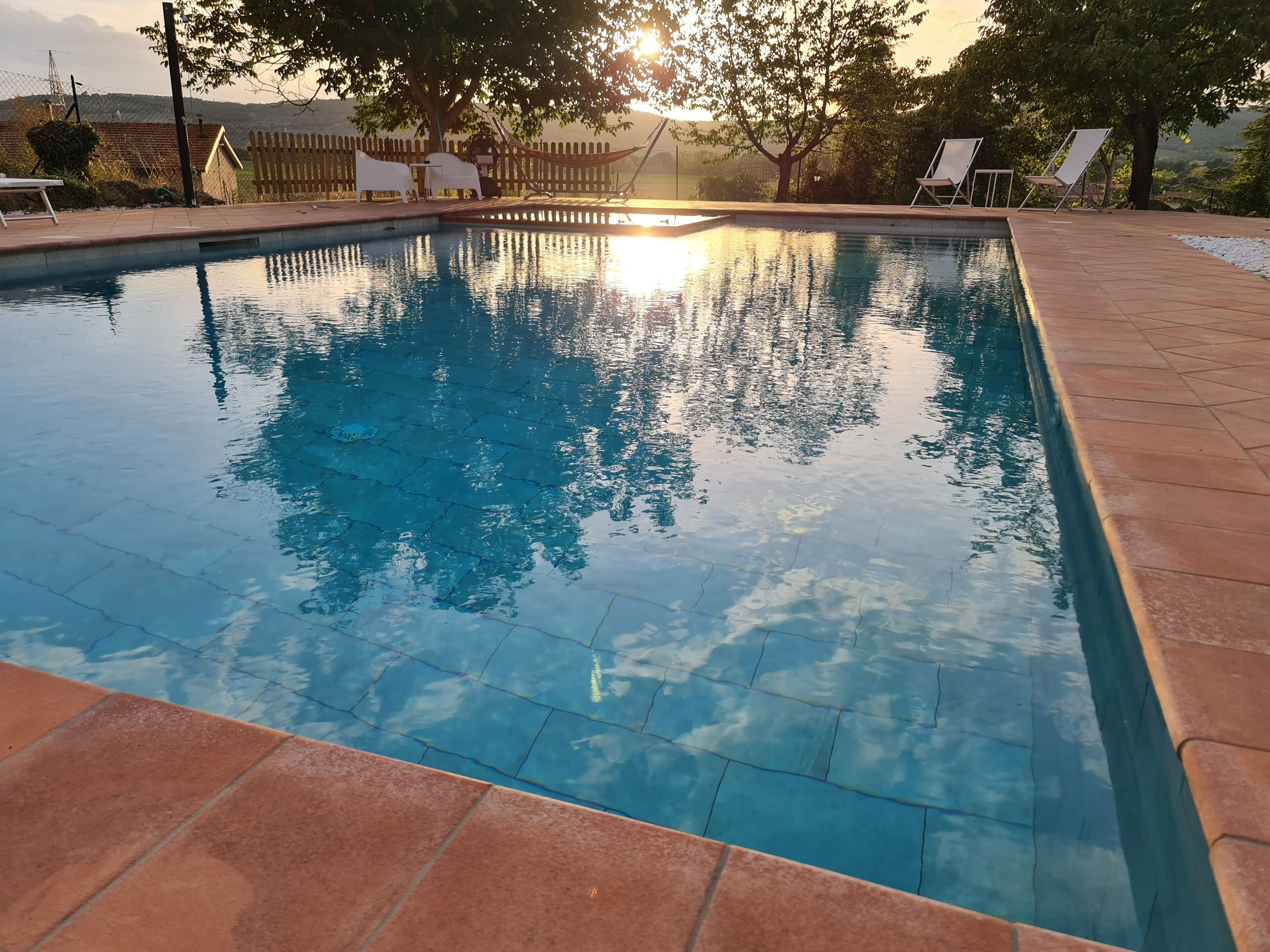 Una piscina rectangular con agua azul cristalina, rodeada por una solana con baldosas y sillas de descanso blancas.