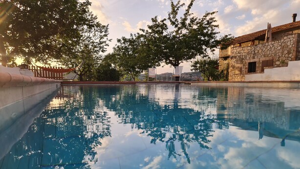 Una piscina con agua cristalina que refleja árboles y un edificio de piedra al fondo.