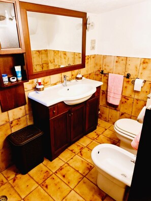 Un baño con tocador de madera, un lavamanos, un espejo, un inodoro y un cubo de basura.