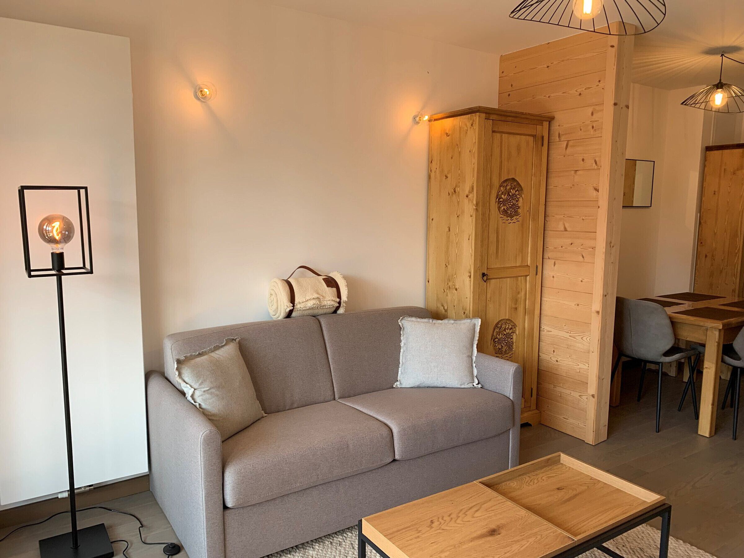 A modern living room with a grey sofa, a wooden cabinet, and a dining area with a table and chairs.