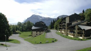 A building with a curved driveway, surrounded by greenery and mountains in the background.