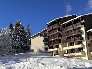 Hotel com vários andares e varandas, rodeado por árvores cobertas de neve.
