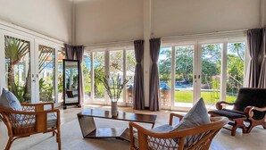 A spacious living area with large glass doors leading to a garden, wicker furniture, and a modern coffee table. - The Backyard Bingin - Cliff Top 10 bedroom Private Villa by Bingin Beach (Pecatu,)