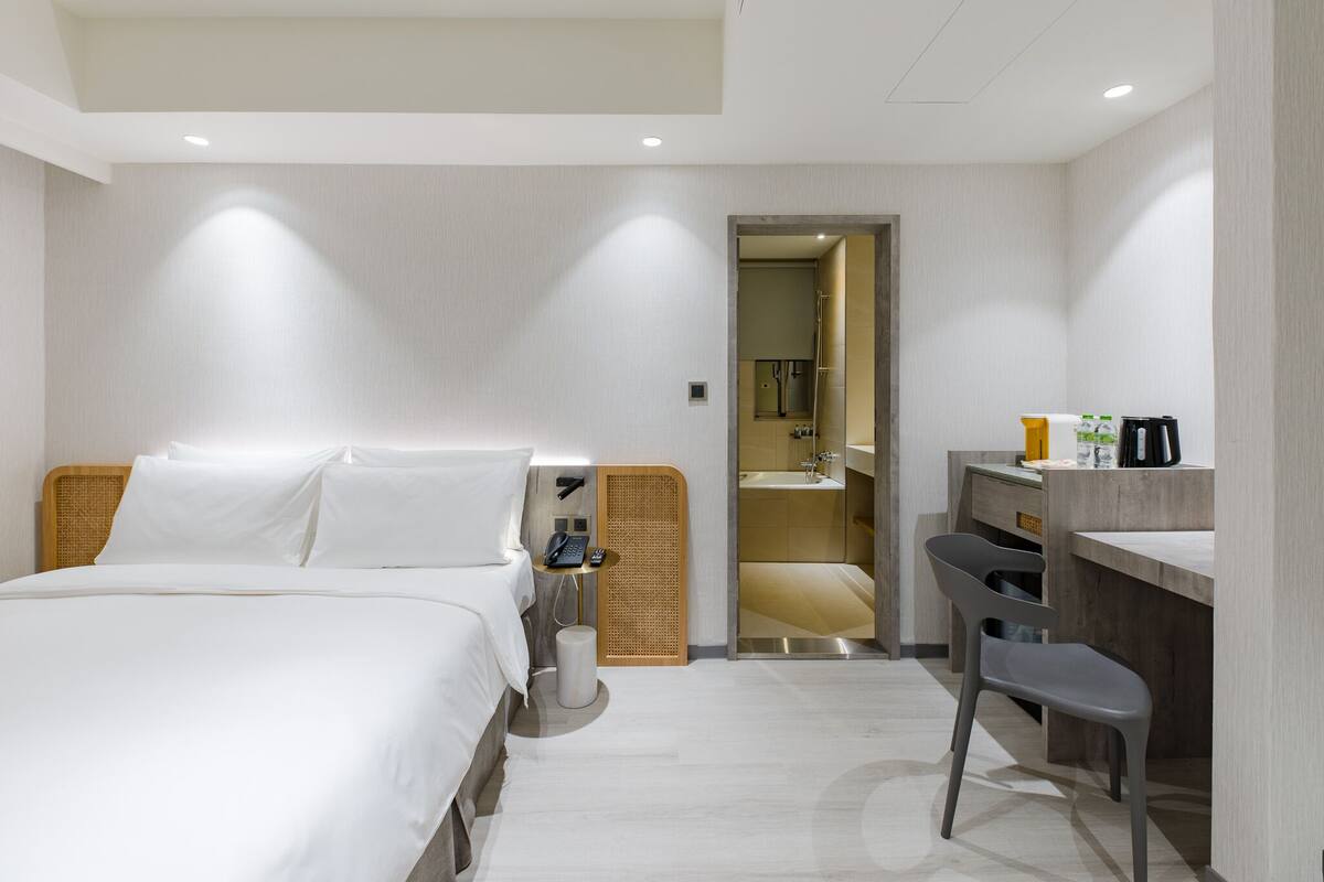 A hotel room with a bed, a desk, a chair, a telephone, and a mirror.