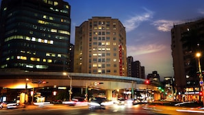 A multi-story building with a prominent central tower, a pedestrian overpass, and a busy intersection with traffic lights. - DAHU Park Hotel (Taipei)