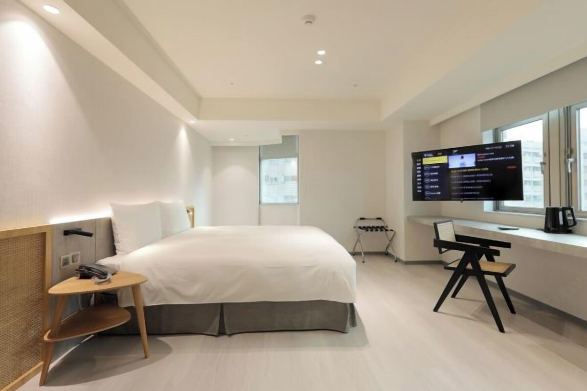 Una habitación de hotel moderna con una cama grande, un escritorio con una silla, un televisor y una ventana.