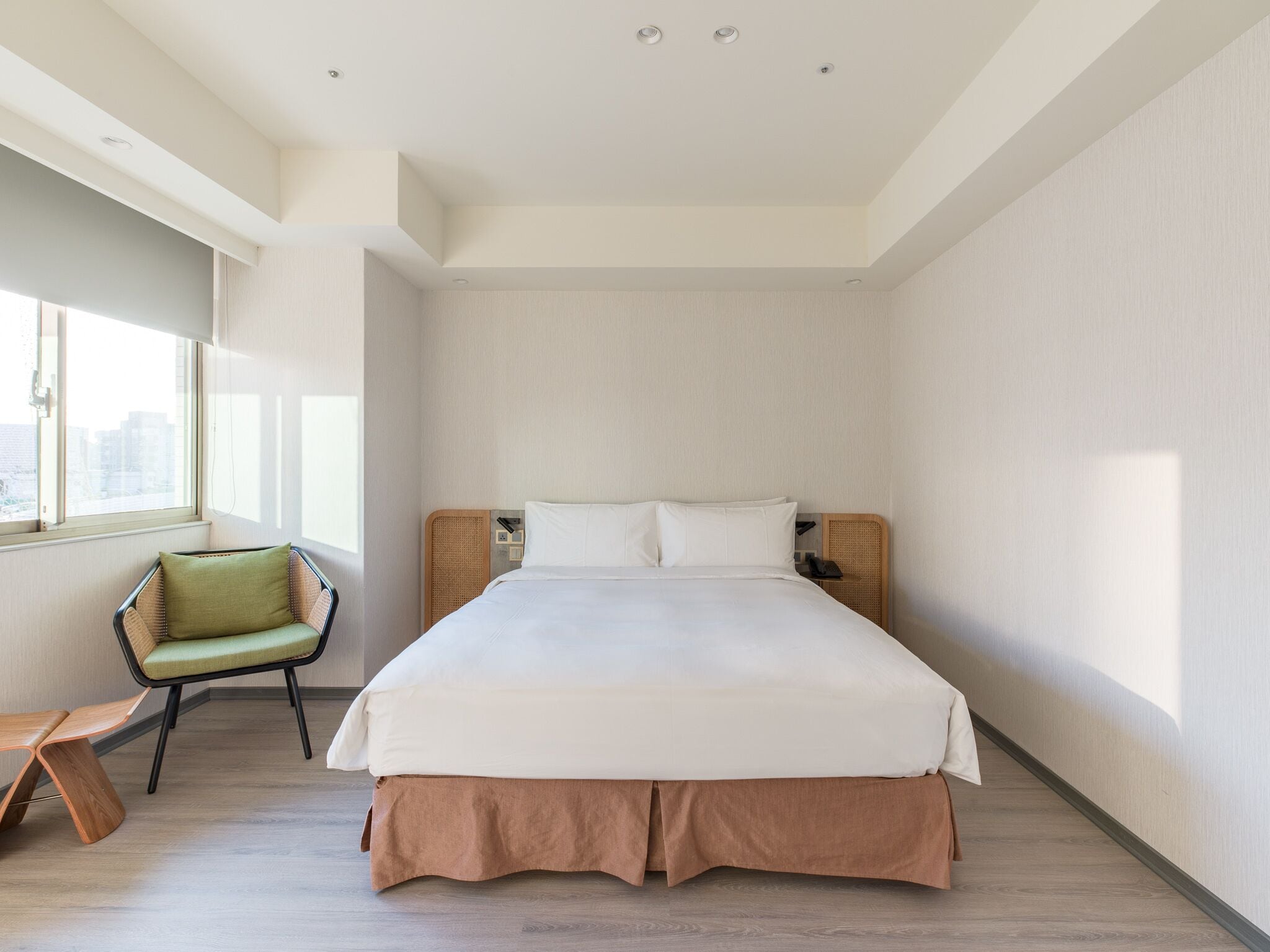 A modern hotel room with a large bed, a green chair, and a view of the city through the window.