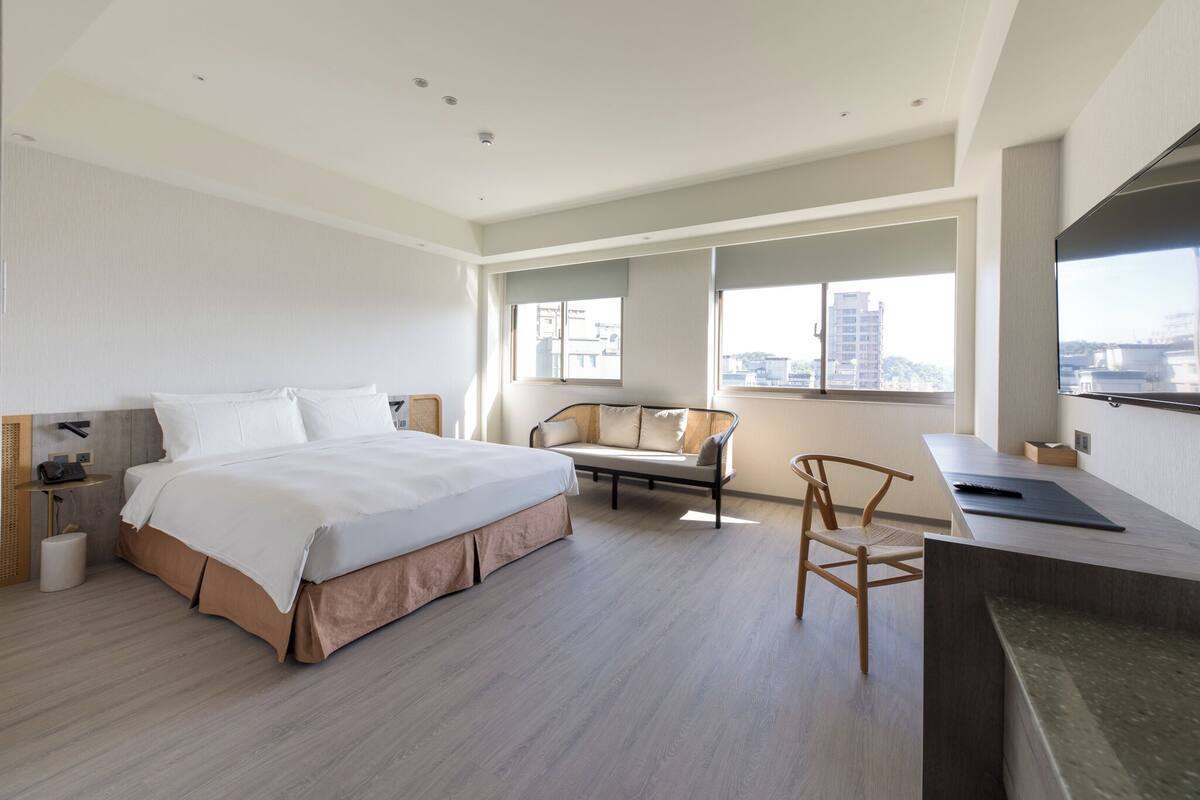 A modern hotel room with a large bed, a sofa, a chair, and a desk.