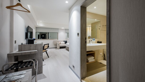 A modern hotel room with a large bed, a desk, a chair, a TV, and a bathroom with a sink and mirror. - DAHU Park Hotel (Taipei)