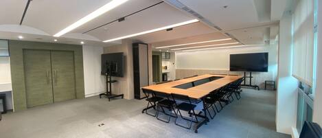 A conference room with a long table, chairs, a TV, and a door.