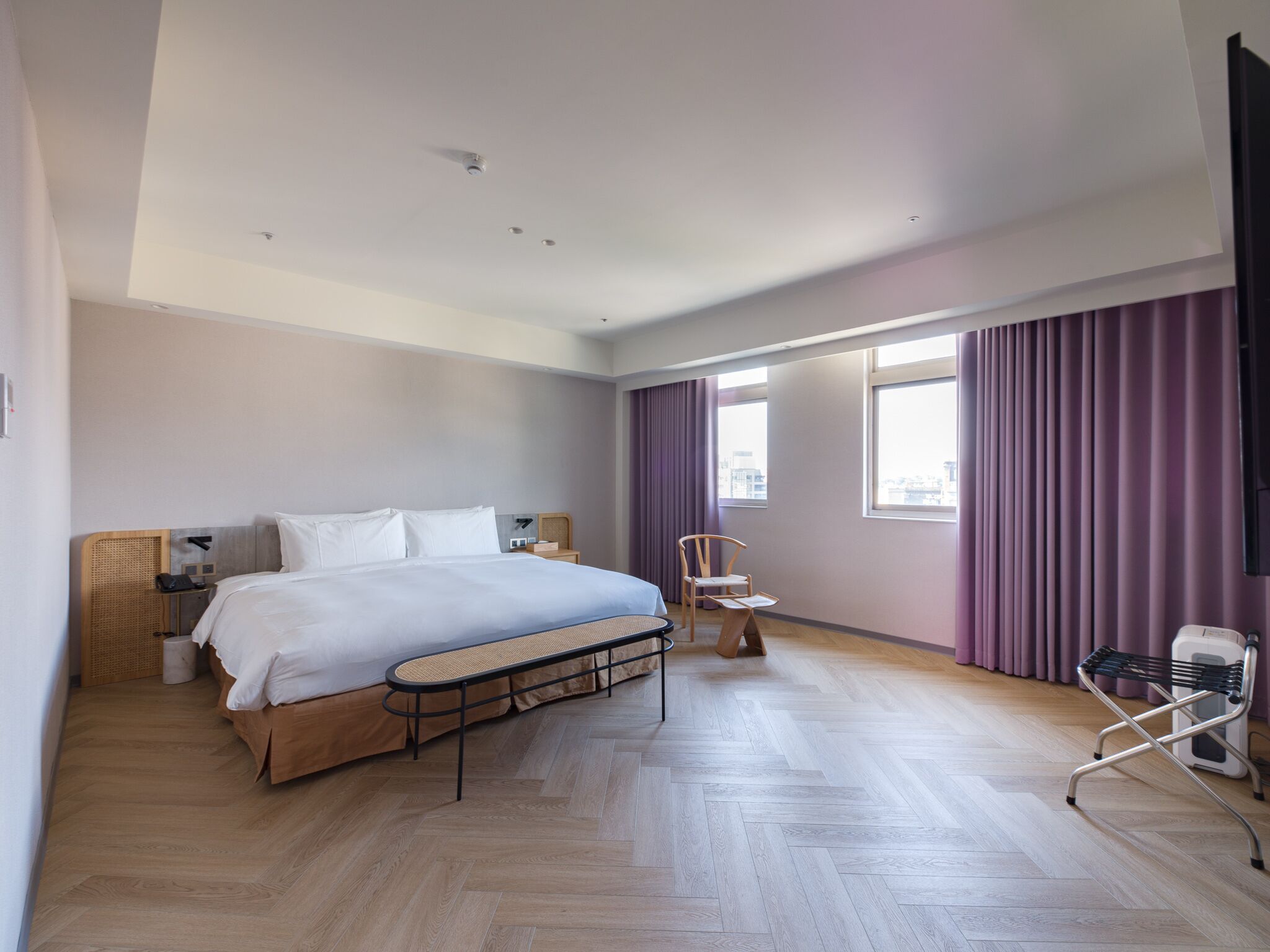 A modern hotel room with a large bed, a small table, a chair, and a TV.