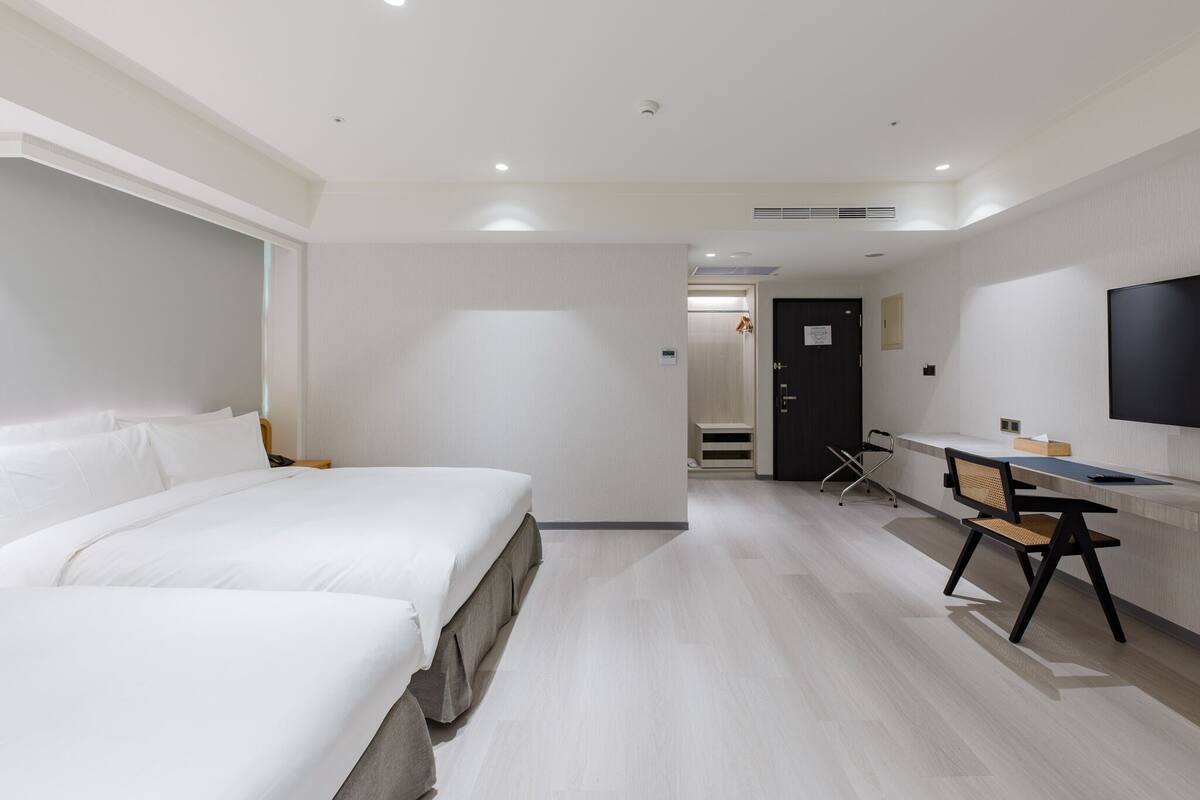A hotel room with two beds, a desk, a chair, a TV, and a door leading to a bathroom.