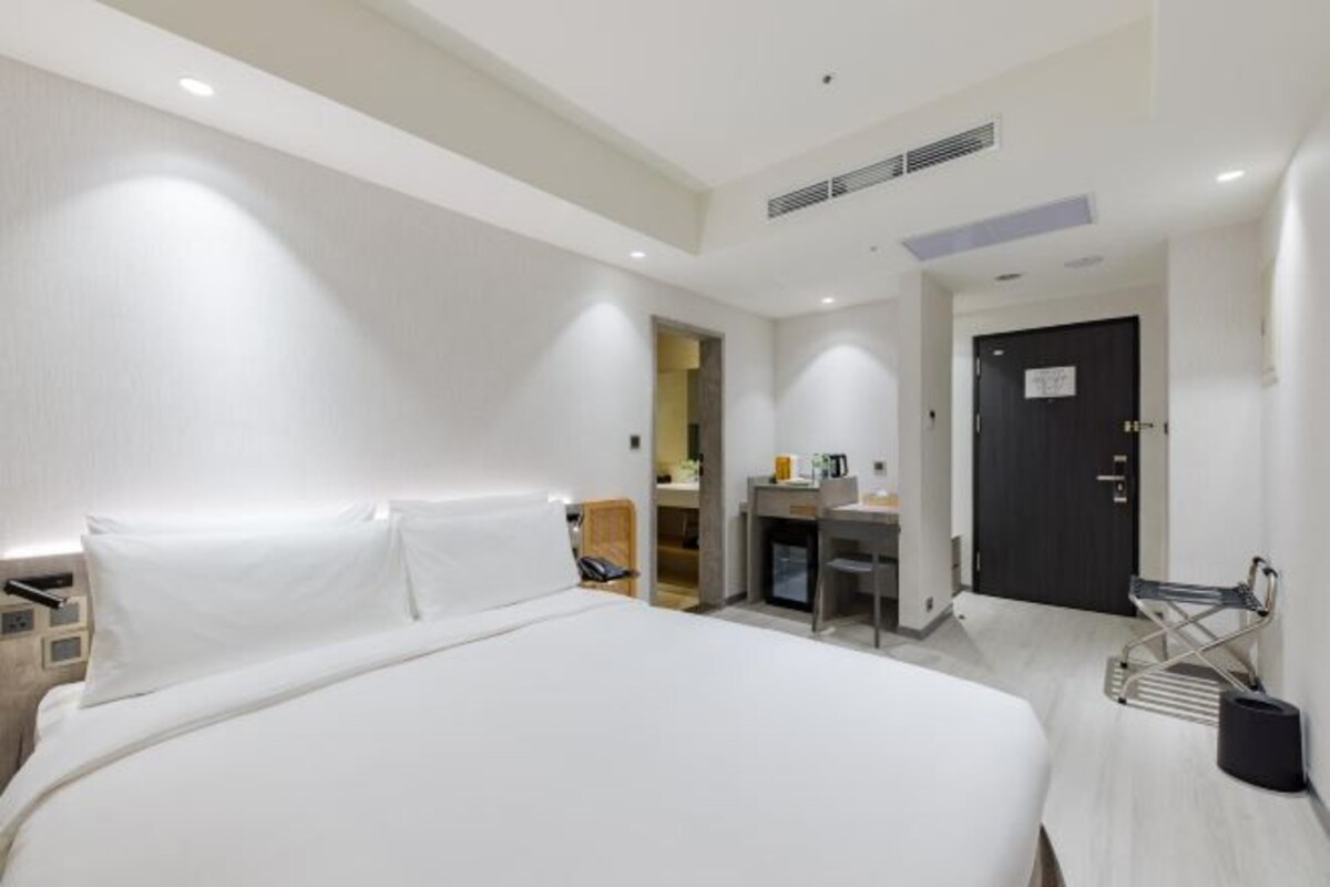 Una habitación de hotel moderna con una cama grande, un escritorio y una pequeña kitchenette.