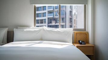 Habitación de hotel con una cama grande, una mesita de noche con teléfono y ventana con vista a edificios.