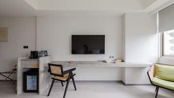 A modern living room with a flat-screen TV mounted on the wall, a dining area with a table and chairs, and a sofa.