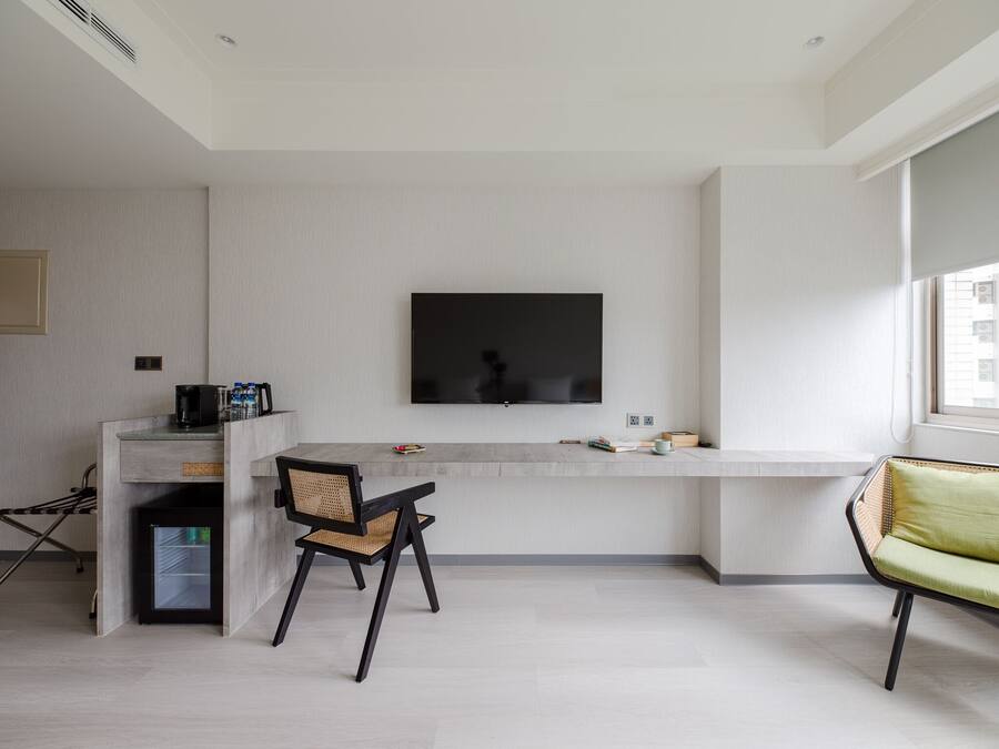 A modern living room with a flat-screen TV mounted on the wall, a dining area with a table and chairs, and a sofa.
