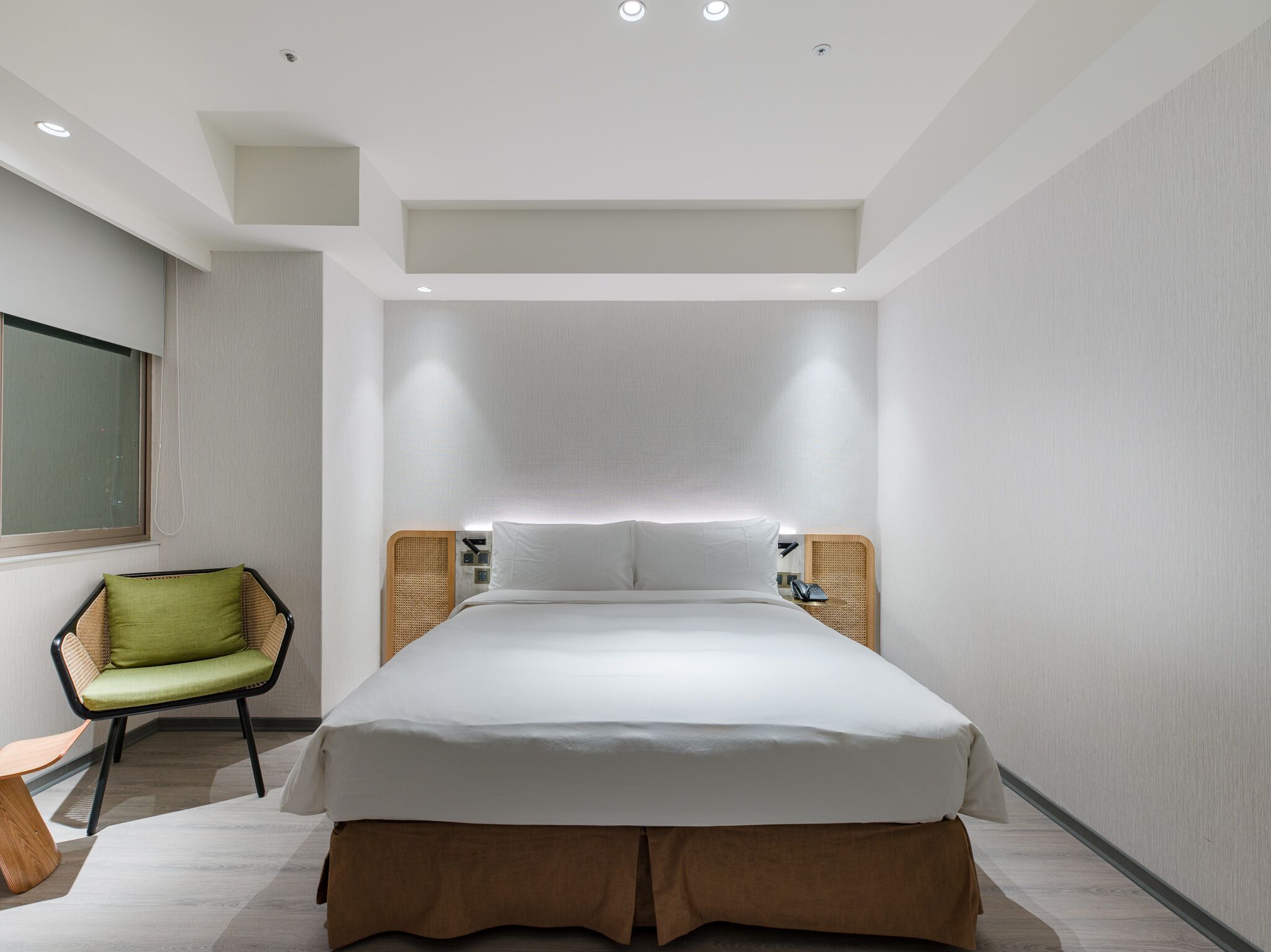 A modern hotel room with a large bed, a green chair, and a bedside table with a lamp.