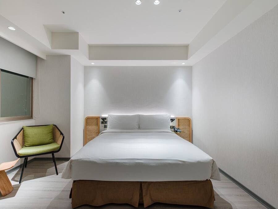 A modern hotel room with a large bed, a green chair, and a bedside table with a lamp.