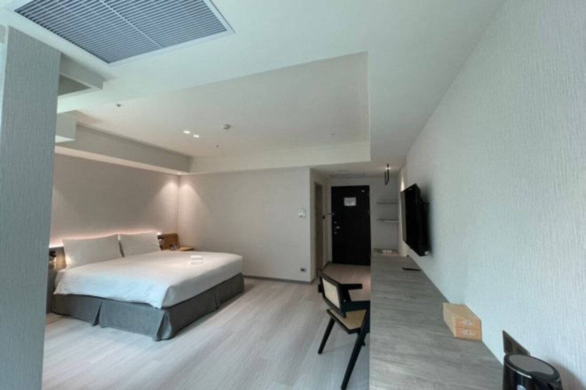 A modern hotel room with a large bed, a desk, and a flat-screen TV mounted on the wall.