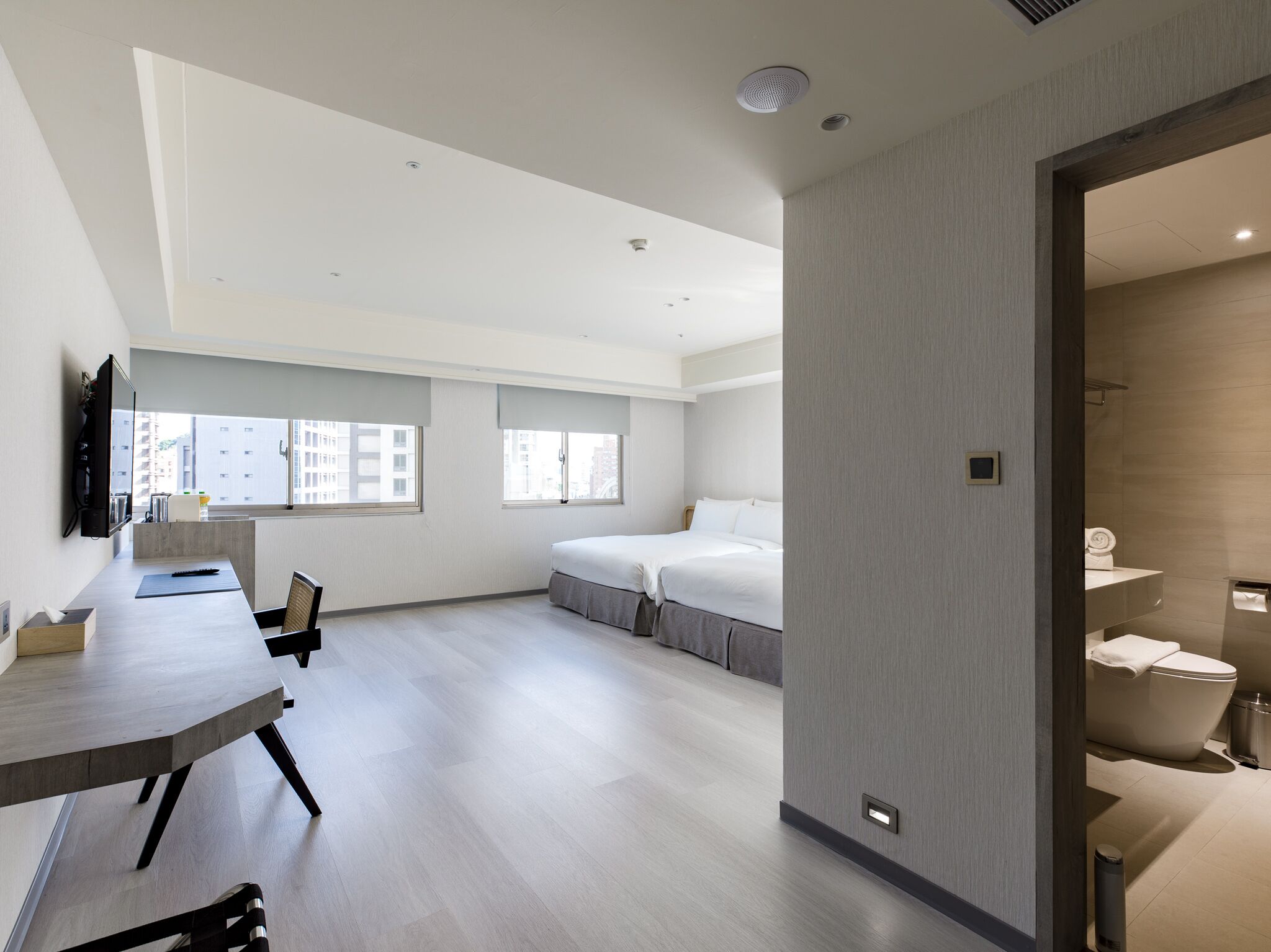A modern hotel room with a large bed, a desk, and a view of the city.