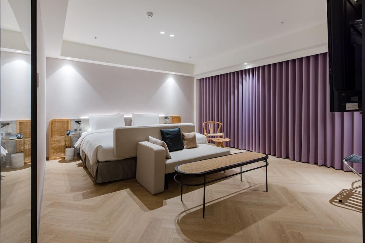 A modern hotel room with a bed, sofa, and a small table.