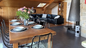 Ein gemütlicher Lofts-Wohnraum mit einem Holzesstisch, gedeckt für vier Personen, einer schwarzen Ledersofa und einem Steinkamin.