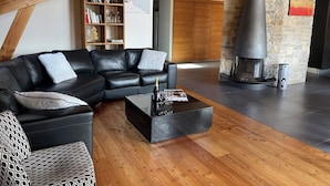 Ein modernes Wohnzimmer mit einem schwarzen Ledersofa, einem Holztisch und einem Kamin aus Stein.