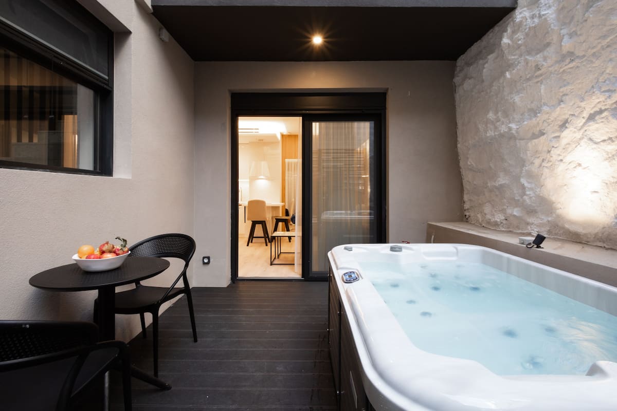 Un espacio exterior moderno con un jacuzzi, una mesa de comedor con sillas y vistas a una habitación con sofá y lámpara.