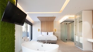 A modern bedroom with a large bathtub, a bed with white linens, and a green wall. - Incanto Suites - Mets (Athens)