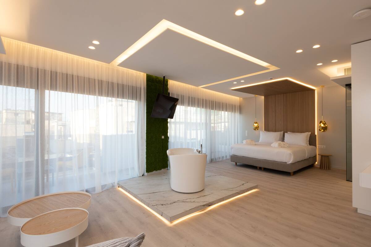 Una habitación de hotel moderna con una cama grande, un área de descanso con una mesa blanca y un televisor montado en la pared.
