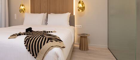 A modern hotel room with a large bed, two pendant lights, a small wooden side table, and a wall with vertical wooden slats.
