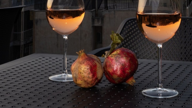 Two wine glasses on a table with pomegranates, overlooking a historic cityscape with ancient ruins. - Incanto Suites - Mets (Athens)