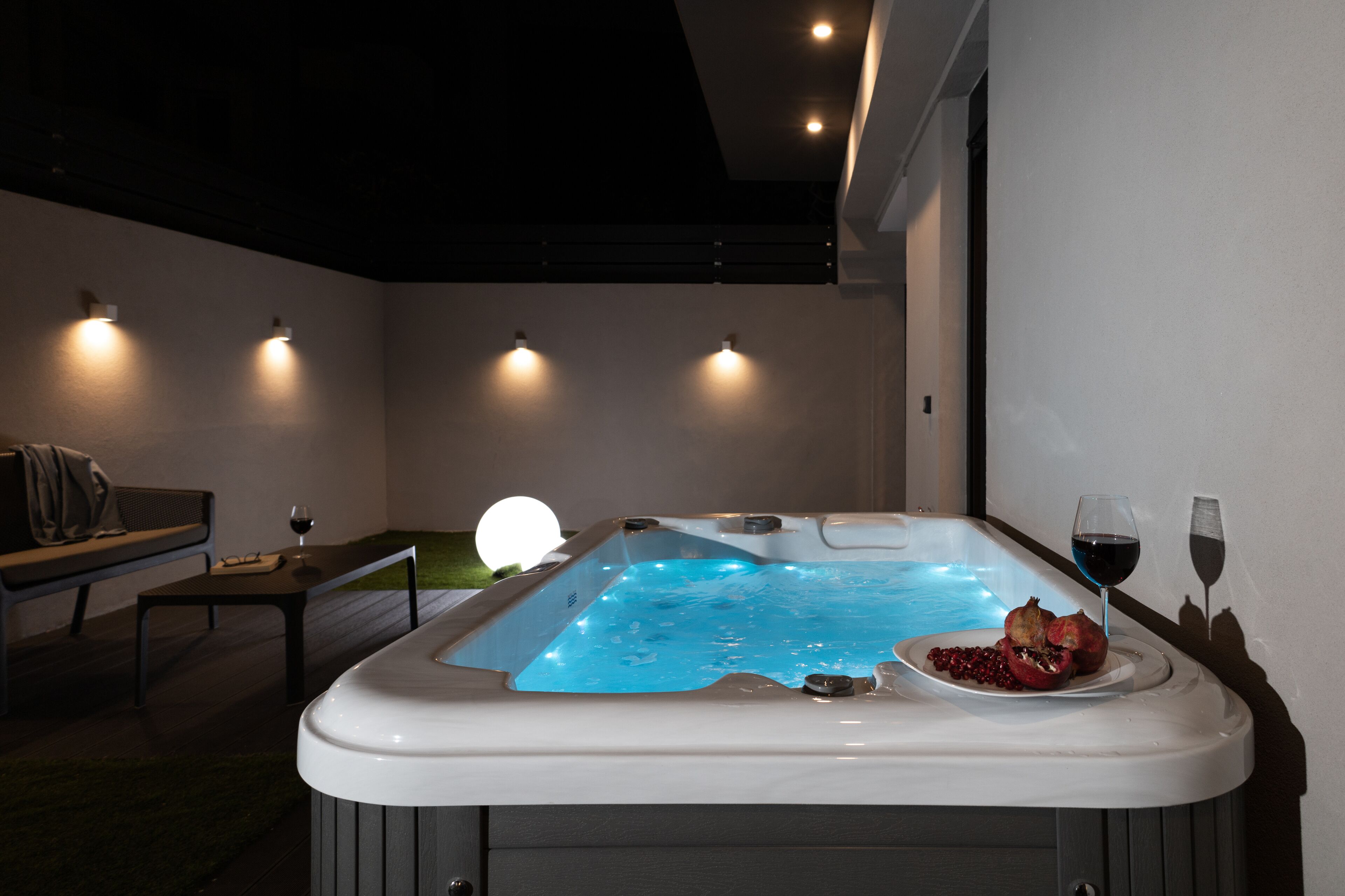 Un moderno spa con una bañera de hidromasaje, un banco y una mesa con una copa de vino y una granada.