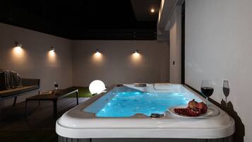 Un moderno spa con una bañera de hidromasaje, un banco y una mesa con una copa de vino y una granada.
