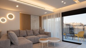 A modern living room with a sectional sofa, two round coffee tables, and a large sliding glass door leading to an outdoor balcony with yellow chairs. - Incanto Suites - Mets (Athens)
