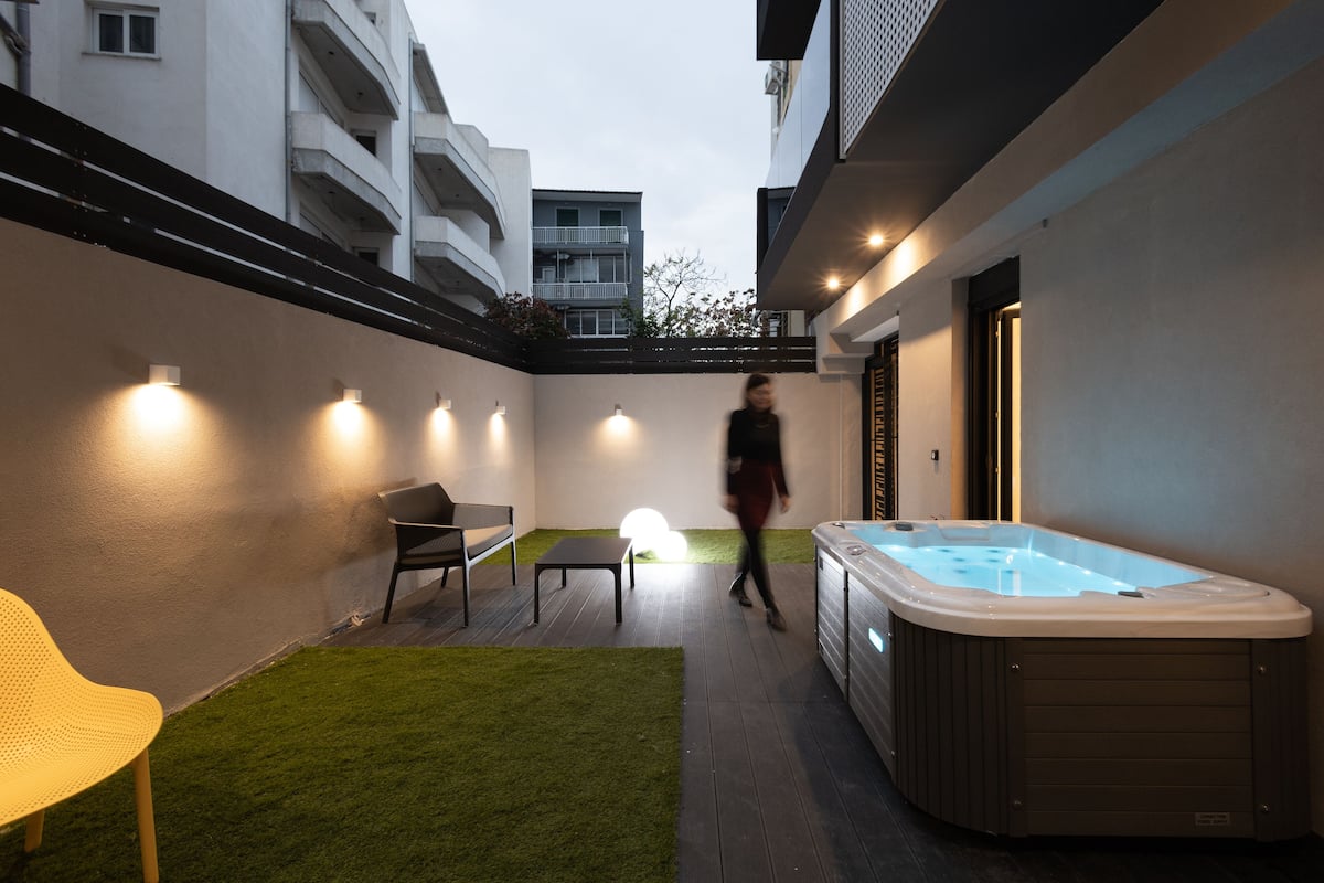 Un patio moderno al aire libre con un jacuzzi, un pequeño césped y una zona de estar.