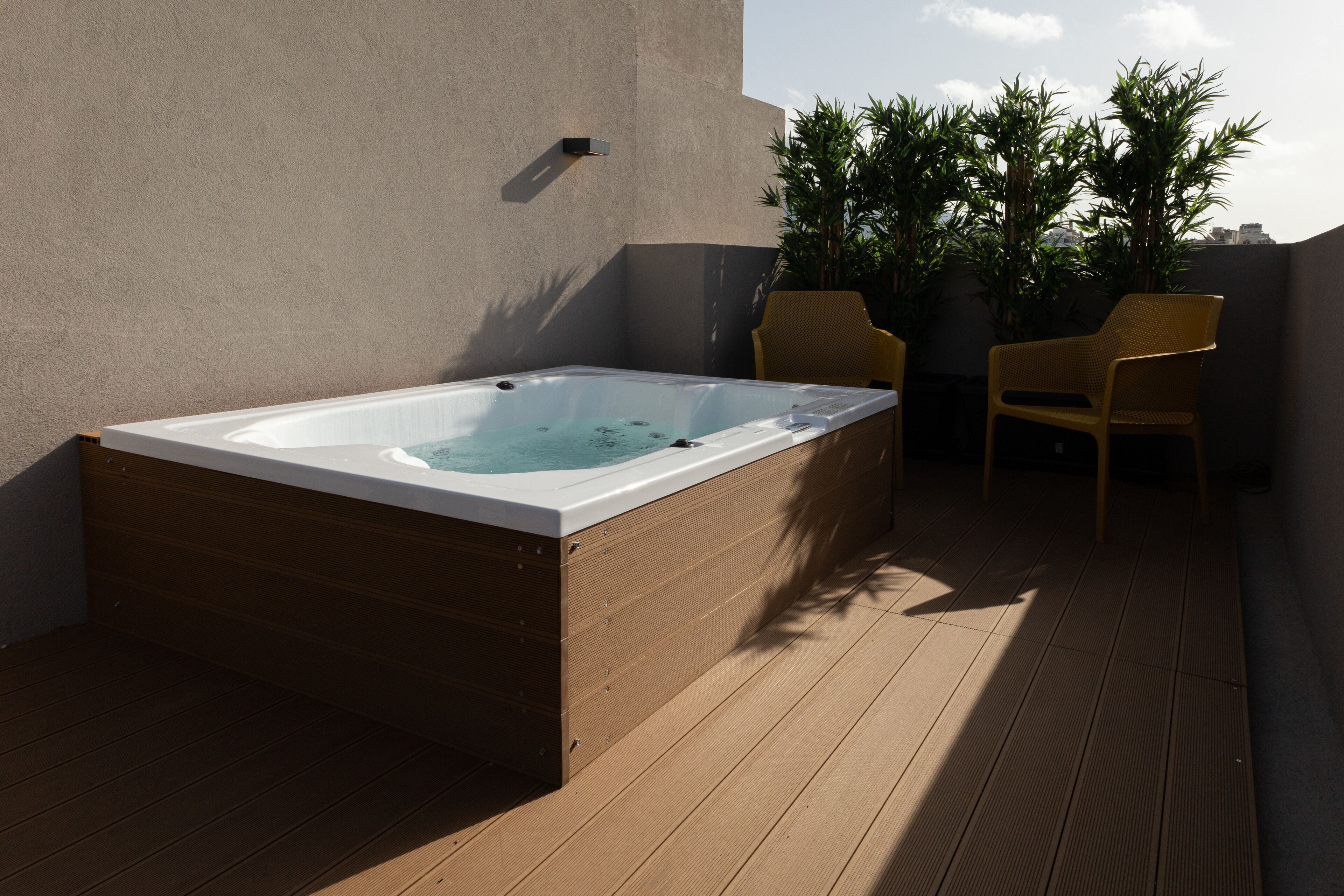 A hot tub on a wooden deck with two chairs and potted plants.