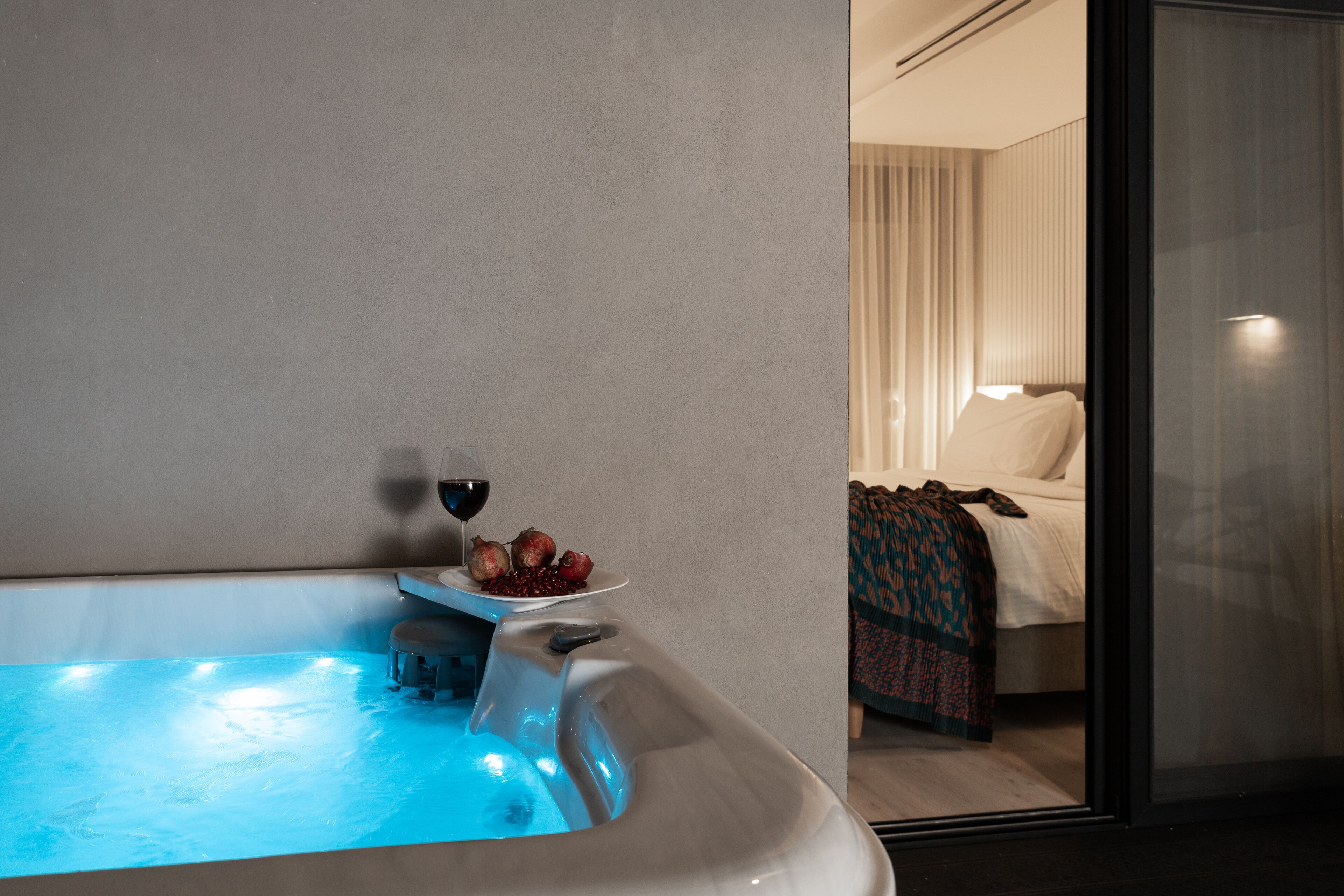 Een moderne hotelkamer met een groot bad, een bed met een geborduurd dekbed en een glazen deur naar een balkon.