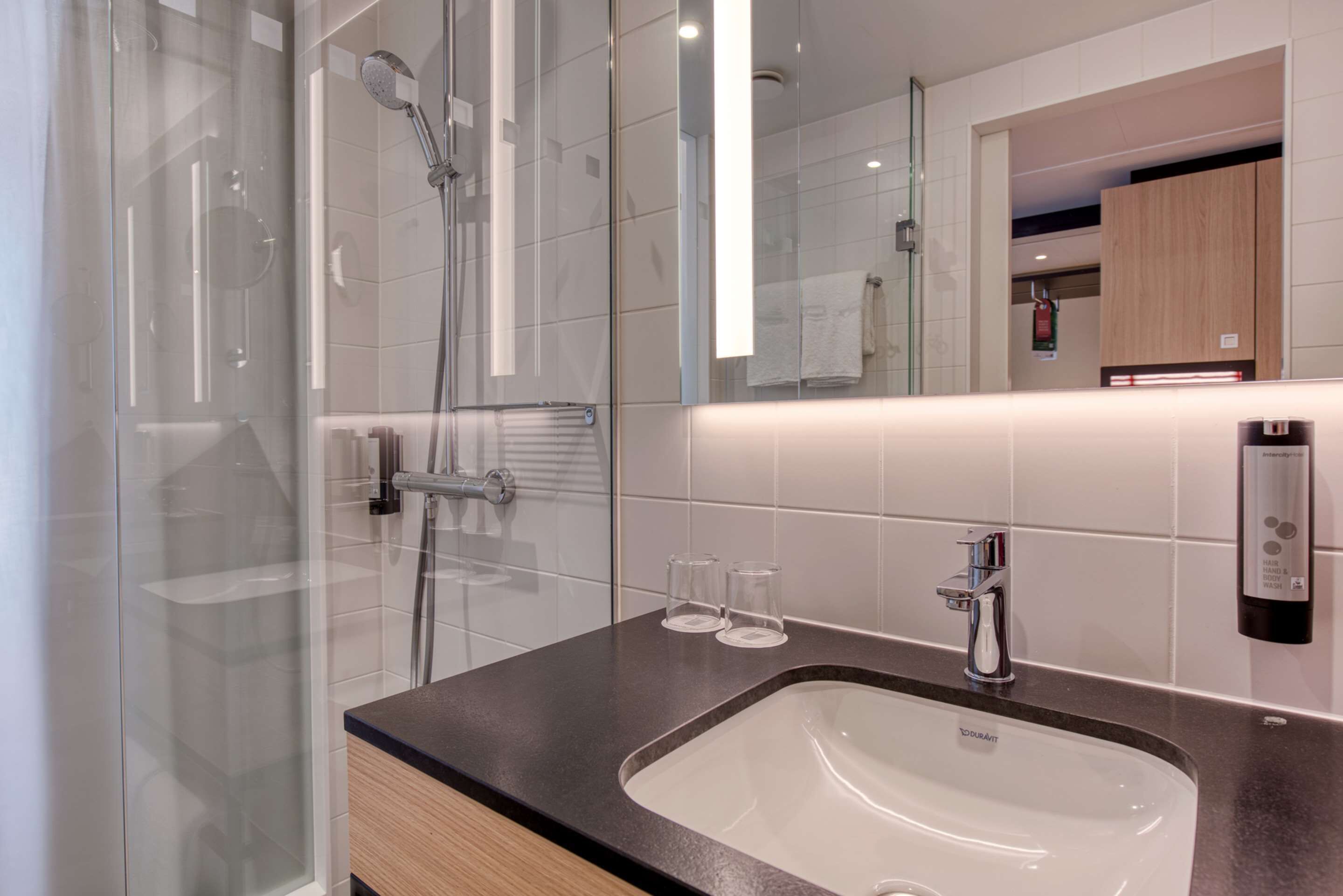 Un baño moderno con ducha envuelta en vidrio, un lavamanos con espejo y un perchero para toallas.