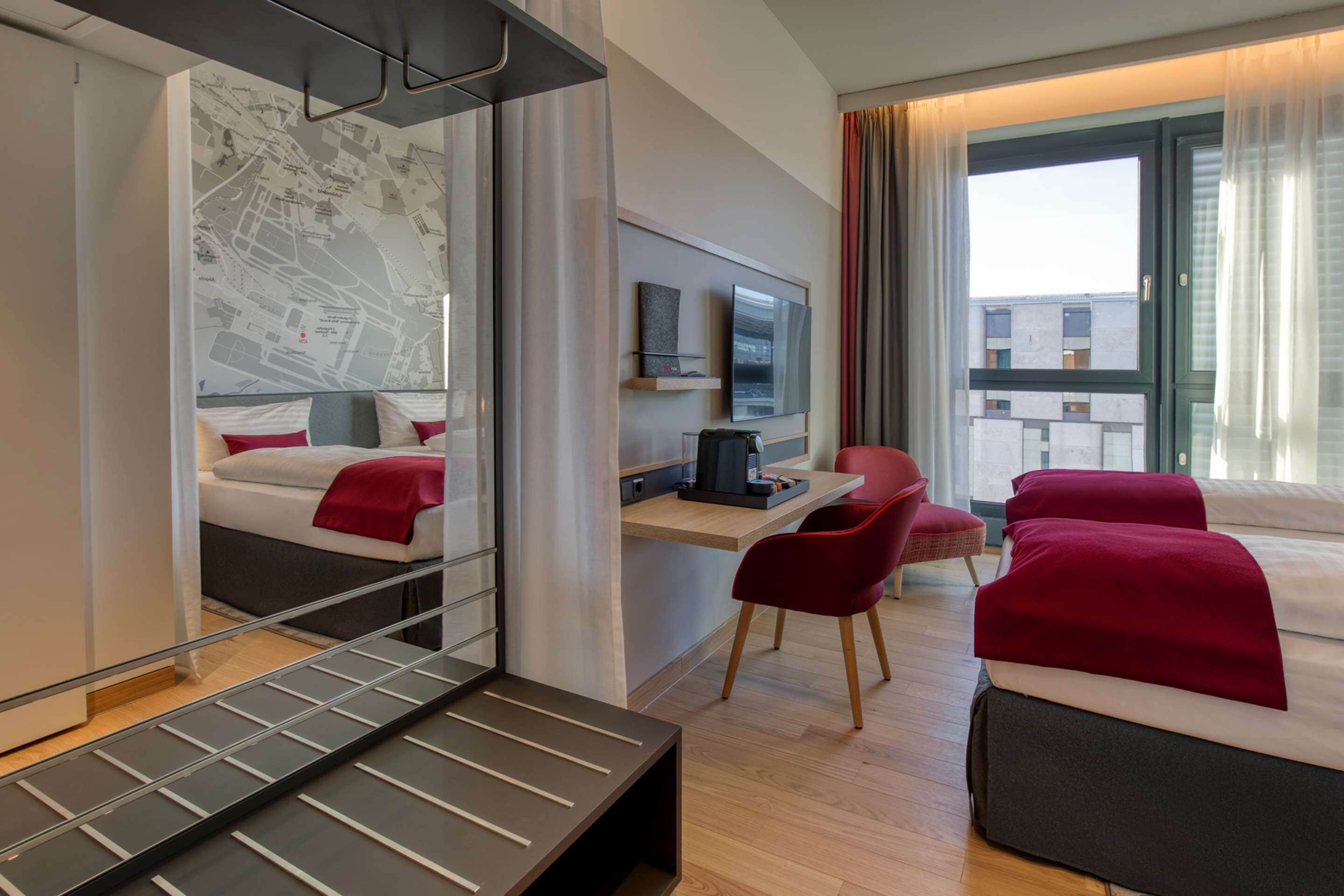 Ein Hotelzimmer mit einem Bett, einem Schreibtisch mit Stuhl, einem Fernseher und einem großen Fenster mit Vorhängen.