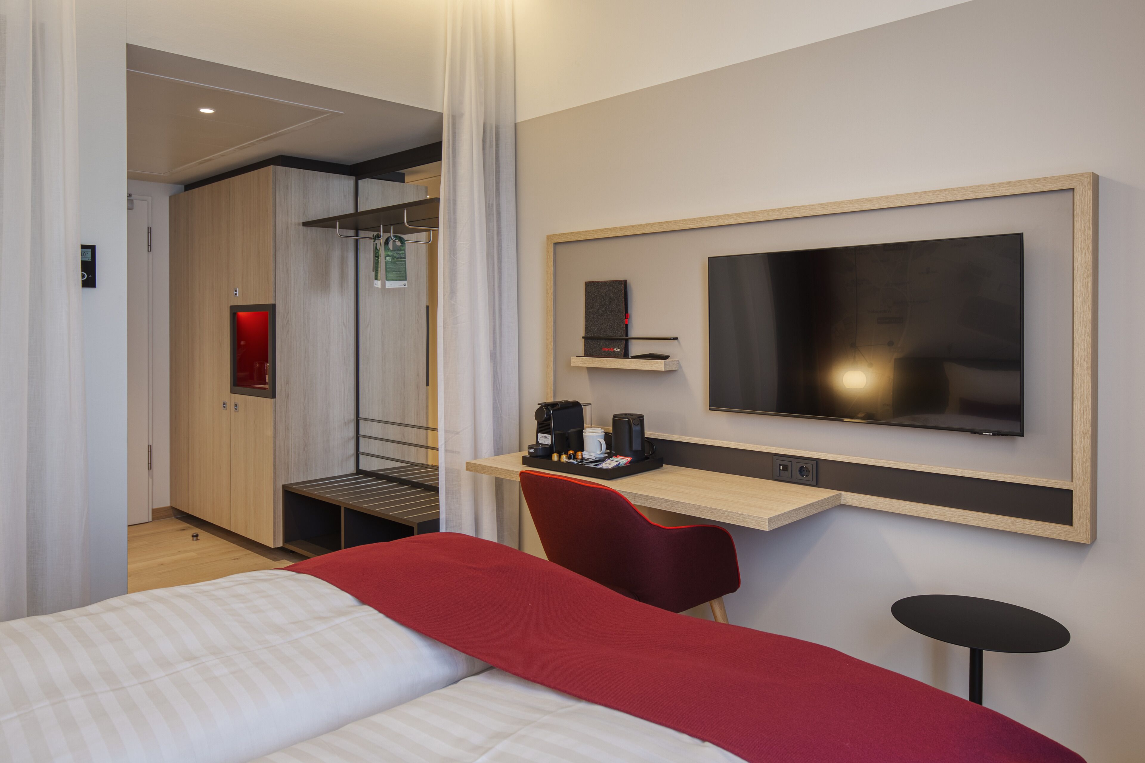 Habitación de hotel con cama, escritorio con silla, televisor y zona de ducha.