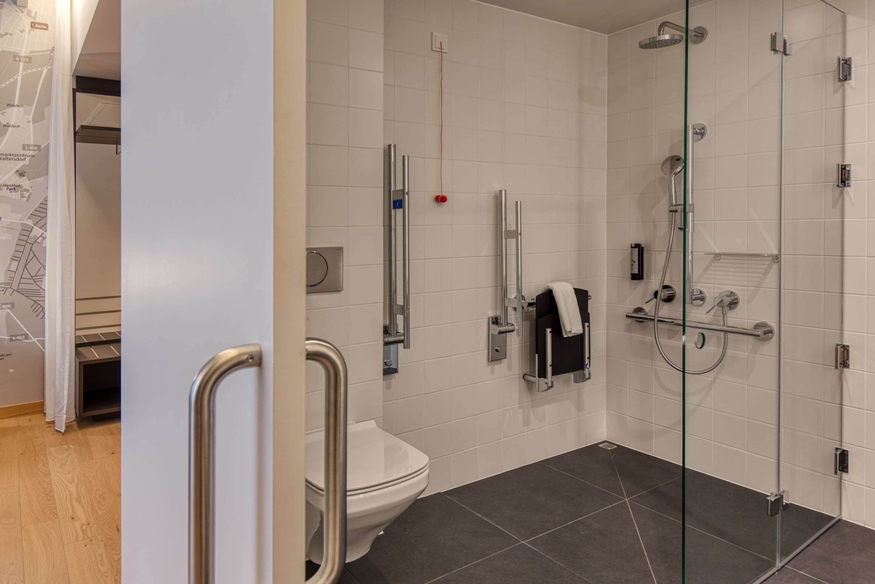 A modern bathroom with a glass shower enclosure, a white toilet, and a handrail.