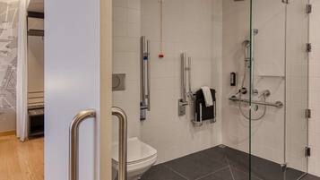 A modern bathroom with a glass shower enclosure, a white toilet, and a handrail.
