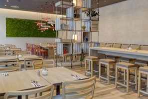 Un restaurante moderno con mesas y sillas de madera, una pared verde y una zona de bar.