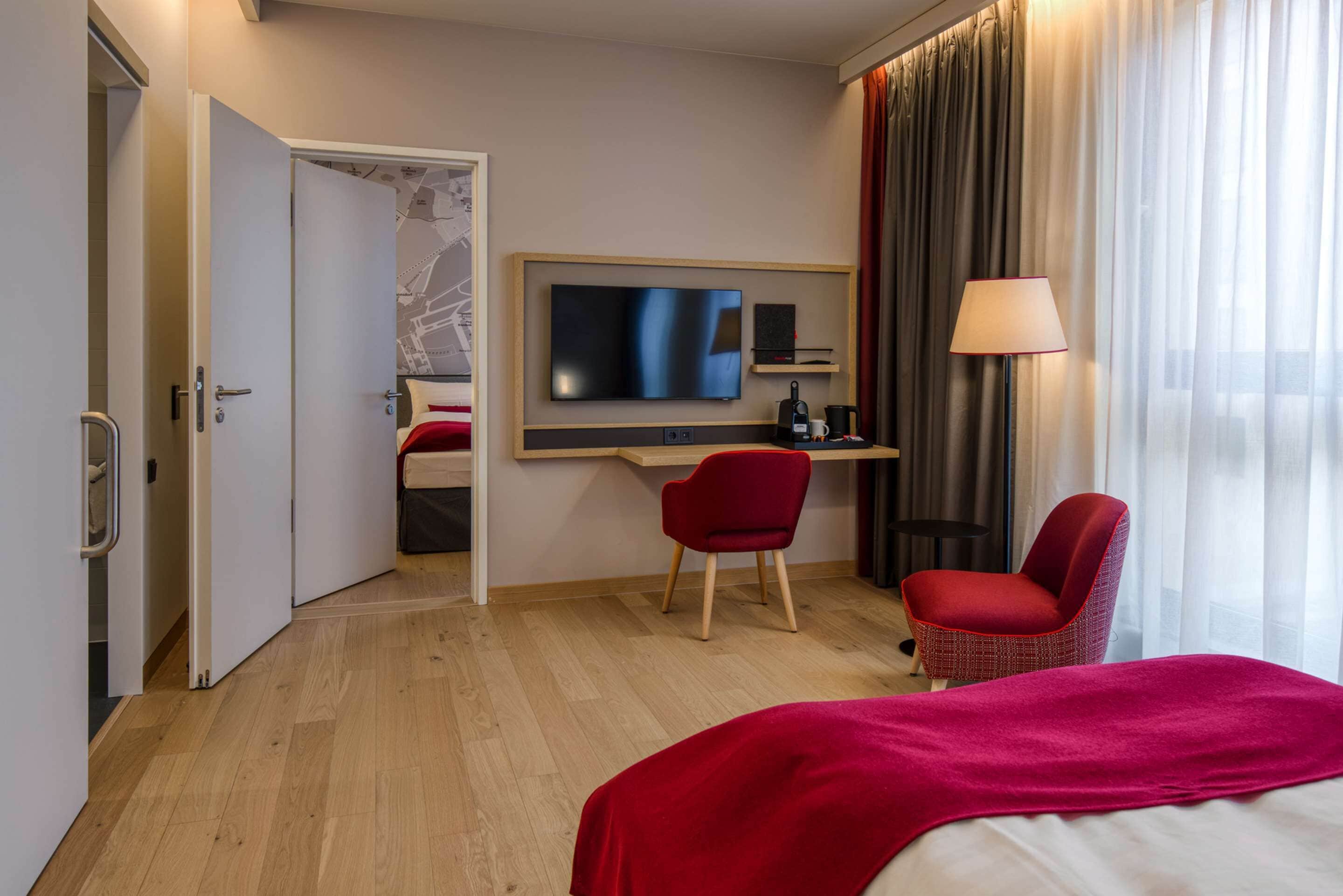 A hotel room with a bed, a desk with a chair, a TV, and a lamp.