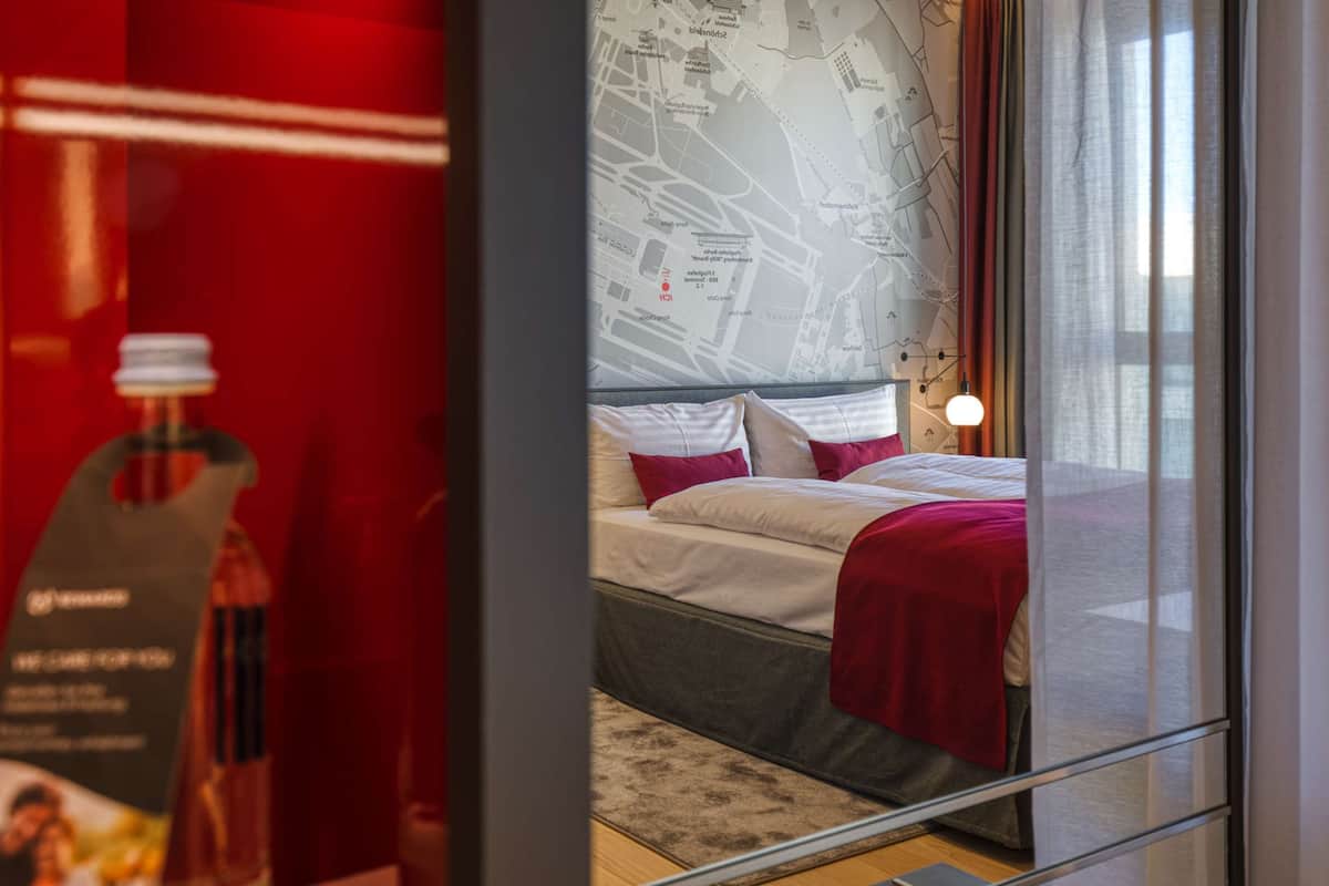 Una habitación de hotel moderna con una cama grande, un mapa en la pared y una pared decorada en rojo.
