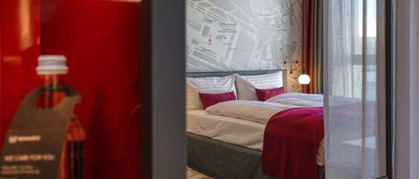 A modern hotel room with a large bed, a map on the wall, and a red accent wall.
