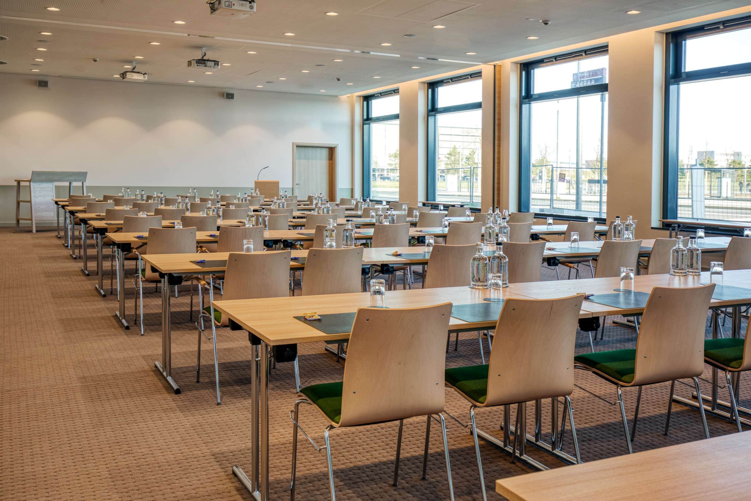 A conference room with rows of tables and chairs, large windows, and a projector screen.